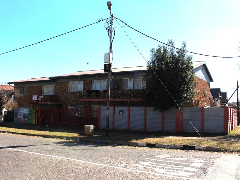 Street view of a multi-story brick apartment building featuring a ground-level retail space and a secure perimeter boundary wall.