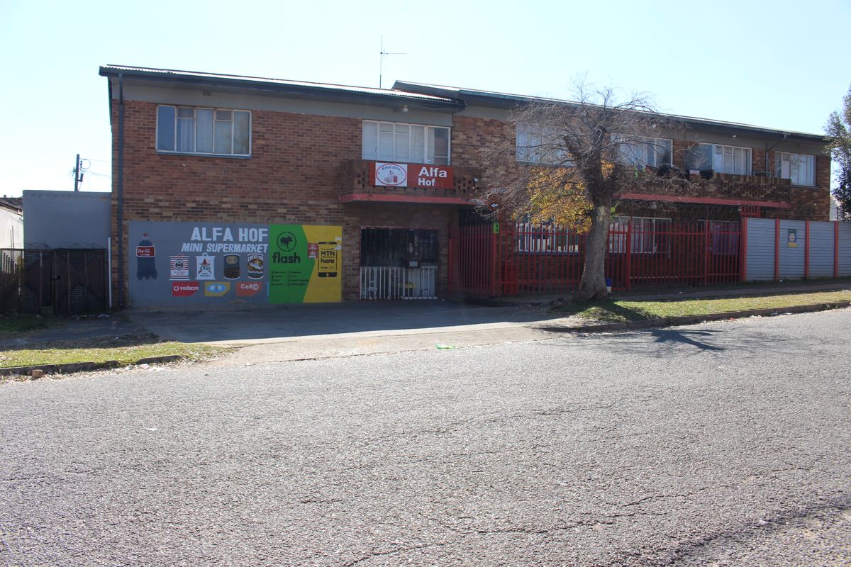 Exterior view of a two-story brick apartment building featuring a ground-floor commercial space and secure metal perimeter fencing.