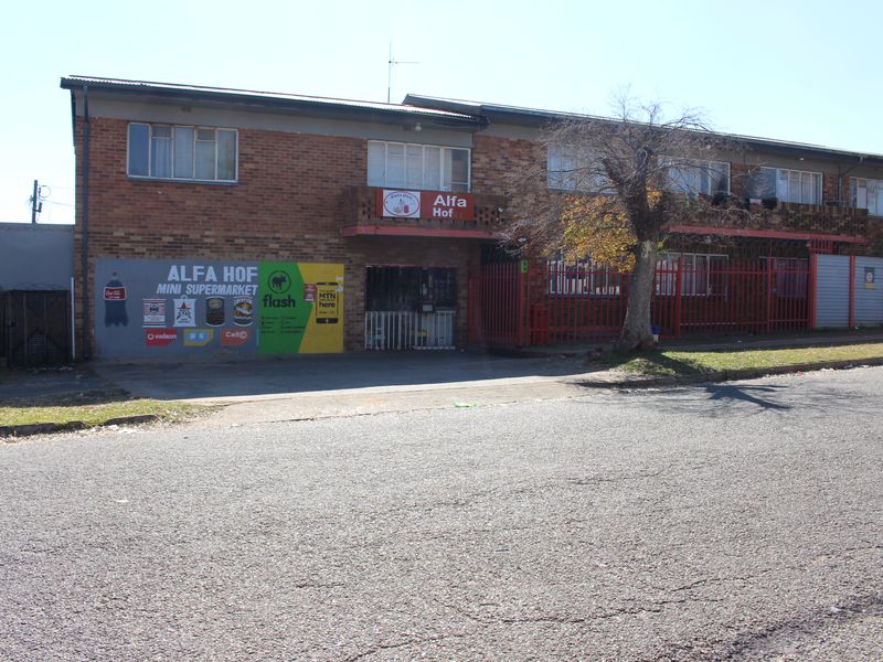 Exterior view of a two-story brick apartment building featuring a ground-floor commercial space and secure metal perimeter fencing.