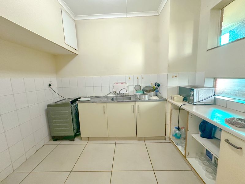 A functional kitchen area featuring tiled flooring, a stainless steel sink, and built-in cabinetry with some open shelving and storage space.