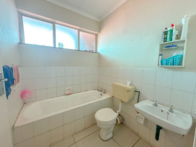 A functional bathroom featuring a bathtub, wall-mounted basin, and toilet with tiled finishes and natural light from an obscured glass window.