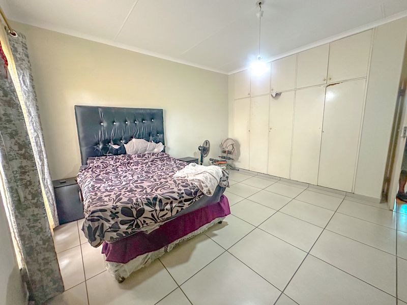 Spacious bedroom featuring large built-in cupboards and neutral tiled flooring, offering a functional layout ready for modern updates.