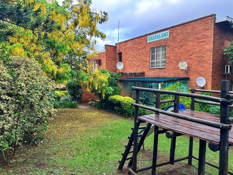 Rear view of the Khayalami apartment complex featuring a brick facade, established garden, and communal outdoor space.