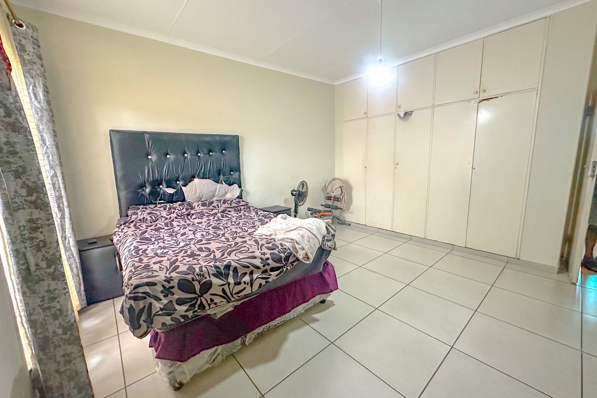 Spacious bedroom featuring large built-in cupboards and neutral tiled flooring, offering a functional layout ready for modern updates.