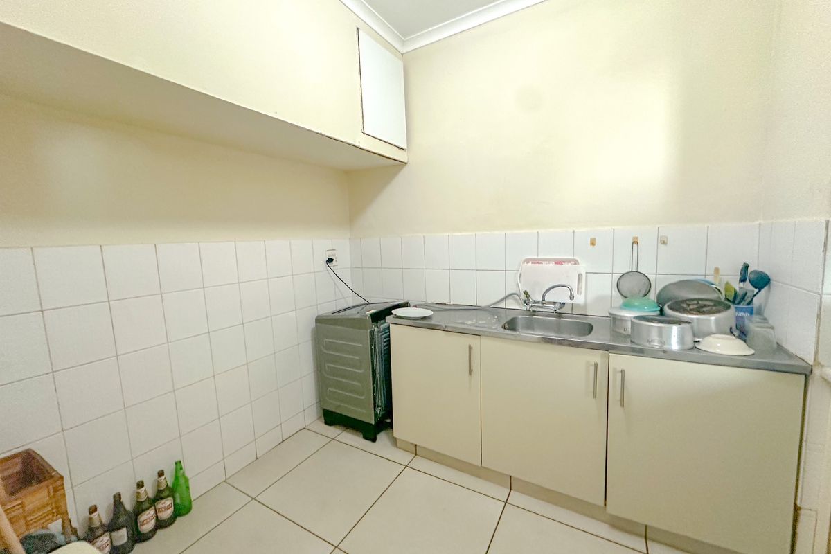 A compact kitchen area featuring basic built-in cabinetry, a stainless steel sink, and tiled splashbacks, requiring cosmetic updates to improve functionality and aesthetic appeal.