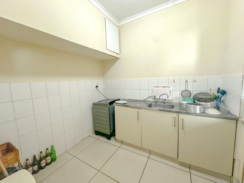 A compact kitchen area featuring basic built-in cabinetry, a stainless steel sink, and tiled splashbacks, requiring cosmetic updates to improve functionality and aesthetic appeal.