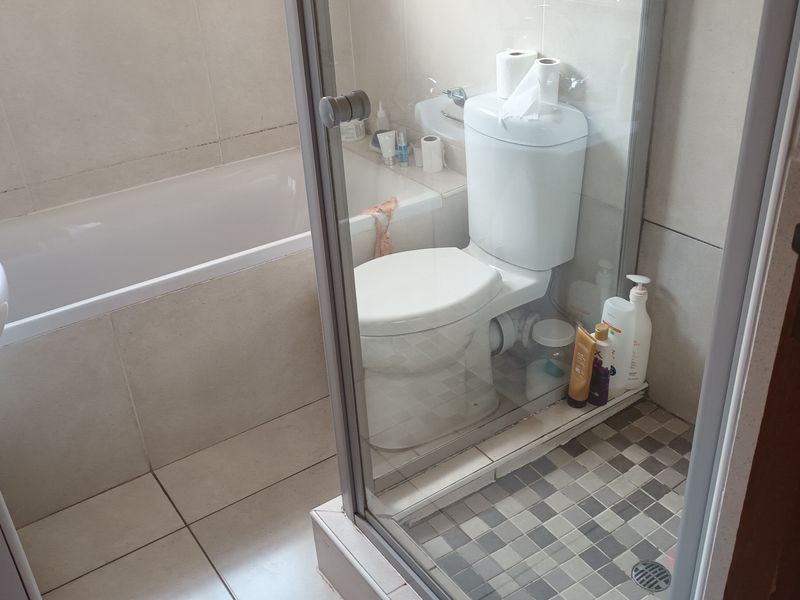 A functional bathroom featuring a bathtub, a separate shower enclosure, a pedestal basin, and neutral wall and floor tiling.