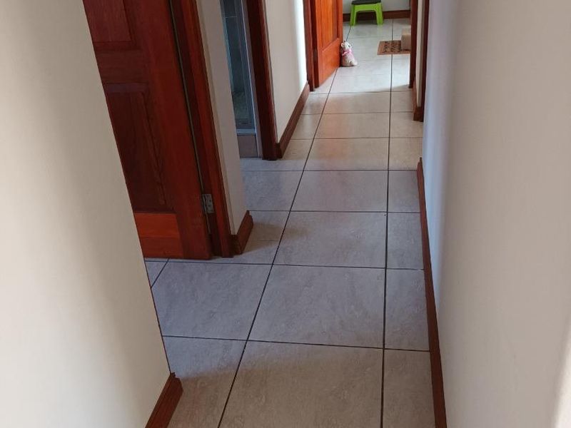 A clean, well-maintained hallway featuring neutral floor tiles and classic wooden door frames leading to adjacent rooms.