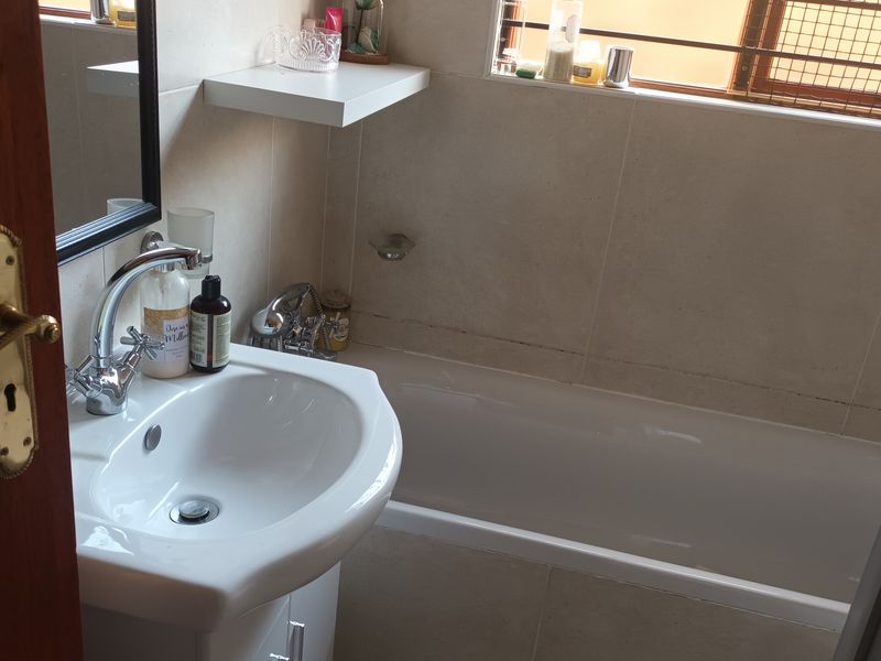 A functional bathroom featuring a pedestal basin with chrome mixer tap, a built-in bathtub, and neutral wall tiling.