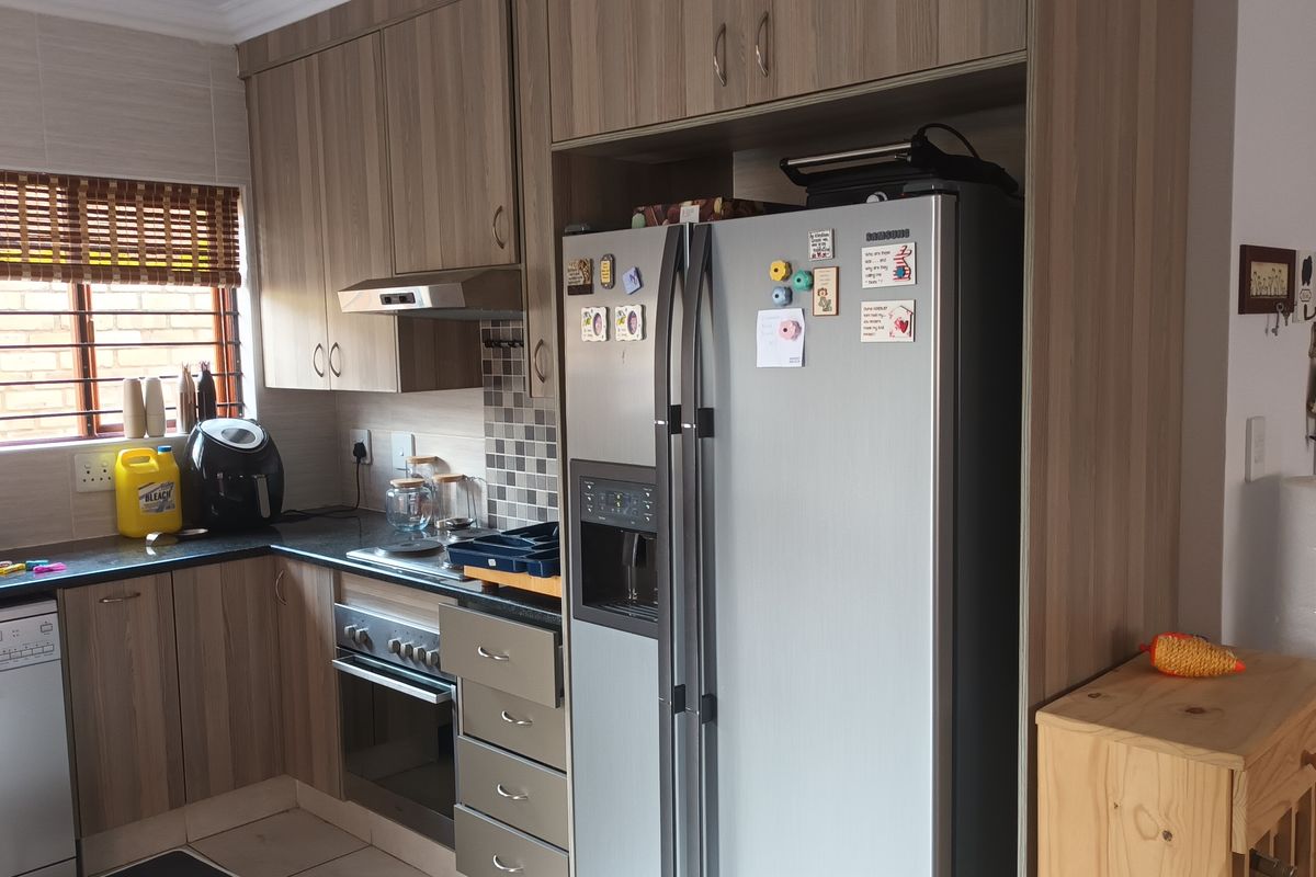 A functional kitchen featuring wood-look cabinetry, mosaic tile backsplash, built-in oven with extractor fan, and dedicated housing for a large double-door refrigerator.