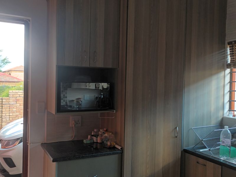 A functional scullery area featuring wood-look built-in cabinetry, laminate countertops, and a stainless steel sink, with direct access to the exterior.