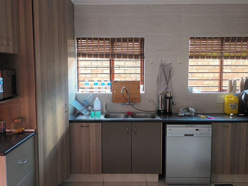 A functional kitchen featuring wood-finish cabinetry, granite countertops, a double basin sink, and integrated appliances including a dishwasher and oven.