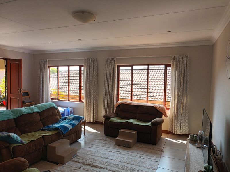 A spacious living room featuring tiled flooring, recessed ceiling lighting, and large windows with wooden frames, offering a bright and functional living space.