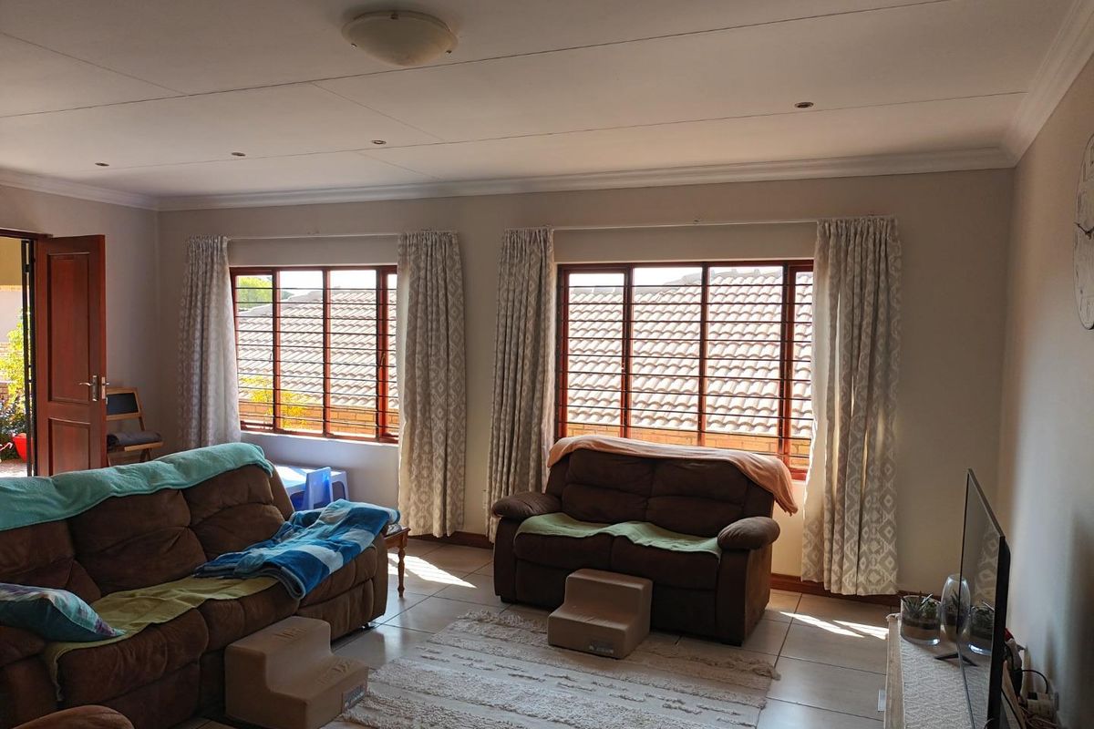 A spacious living room featuring tiled flooring, recessed ceiling lighting, and large windows with wooden frames, offering a bright and functional living space.