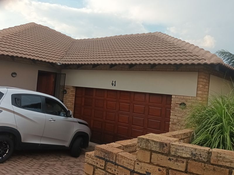 Front elevation of a cluster home featuring a facebrick facade, tiled roof, and a wooden garage door with a paved driveway.