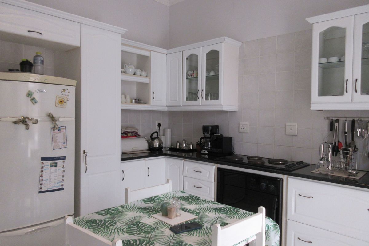 A functional kitchen featuring white cabinetry, black granite countertops, a built-in oven, and an electric hob with a tiled backsplash.