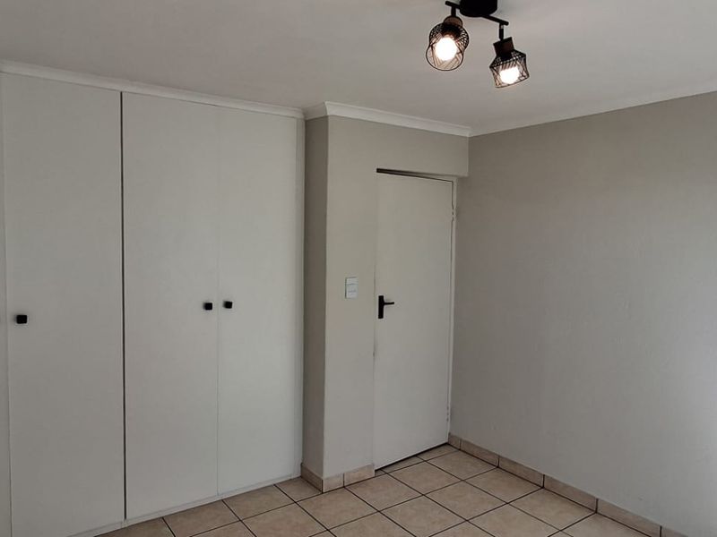 A clean, empty bedroom featuring neutral tiled flooring, built-in white cupboards, and a modern ceiling light fixture.