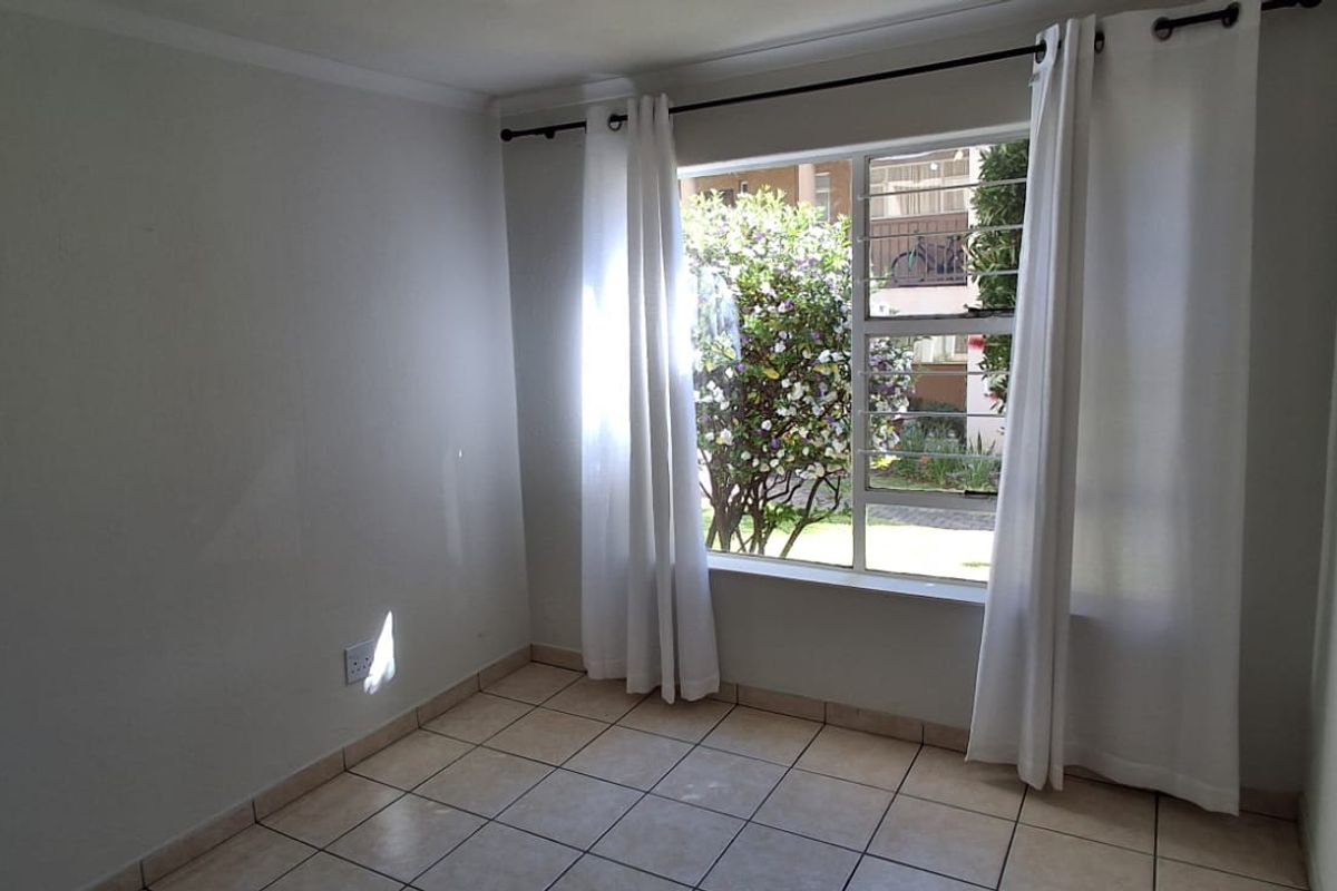 A bright, empty bedroom featuring tiled flooring, neutral walls, and a large window with security bars and curtain fixtures.