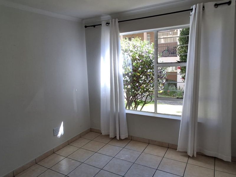 A bright, empty bedroom featuring tiled flooring, neutral walls, and a large window with security bars and curtain fixtures.