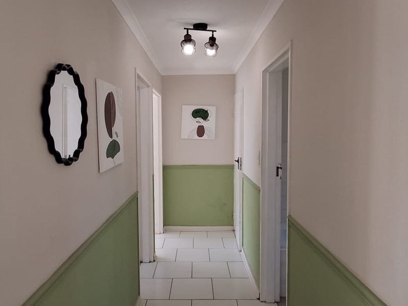 A clean and well-maintained hallway featuring tiled flooring and decorative wainscoting with a neutral and green color palette.