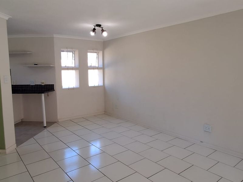 An open-plan living area featuring tiled flooring, neutral walls, and a compact kitchen nook with a built-in counter.