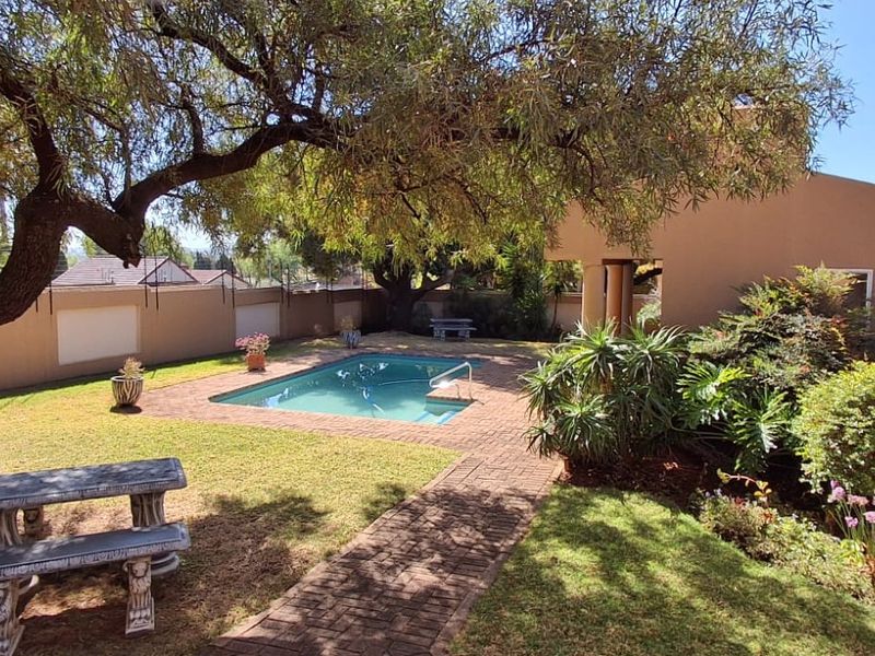 A private outdoor pool area featuring brick paving, established trees, and a secure boundary wall, providing a tranquil space for relaxation.