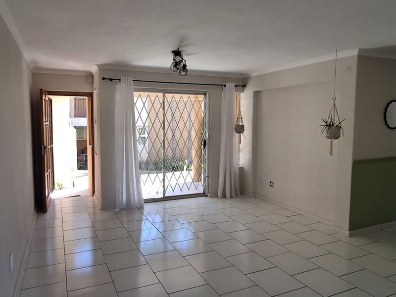 An open-plan living area featuring white tiled flooring, wainscoting, and a sliding glass door with a security gate leading to the exterior.
