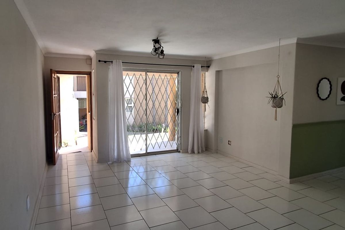 An open-plan living area featuring white tiled flooring, wainscoting, and a sliding glass door with a security gate leading to the exterior.