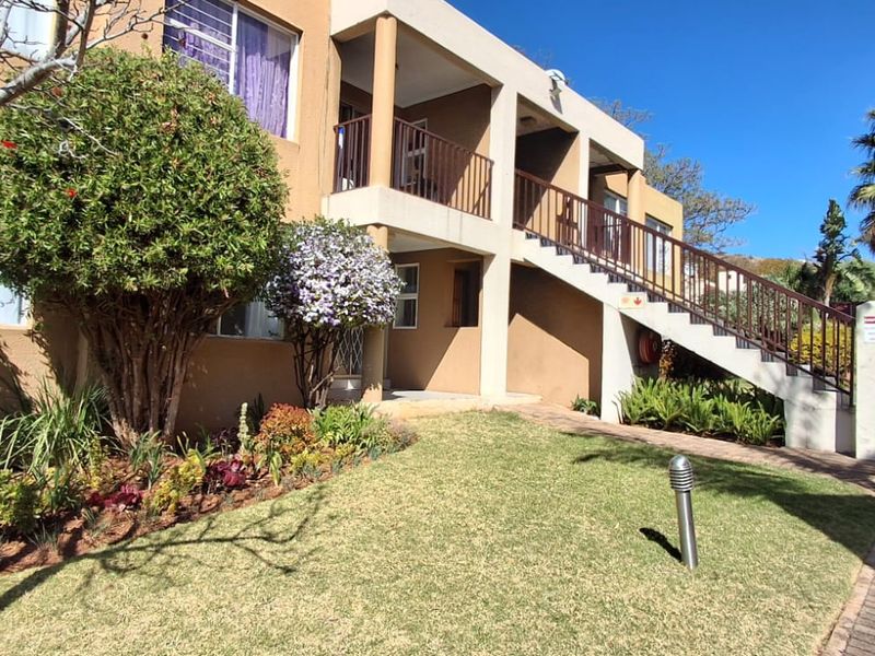 Exterior view of an apartment complex featuring a paved walkway, landscaped garden, and an external staircase leading to upper-level units.