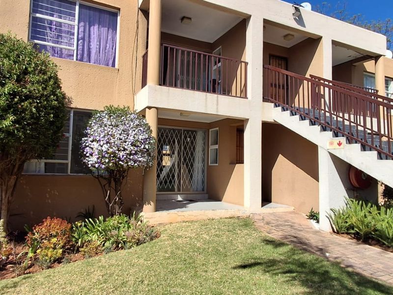 Front exterior view of a multi-story apartment building featuring a paved walkway, landscaped garden, and an external staircase with metal railings.