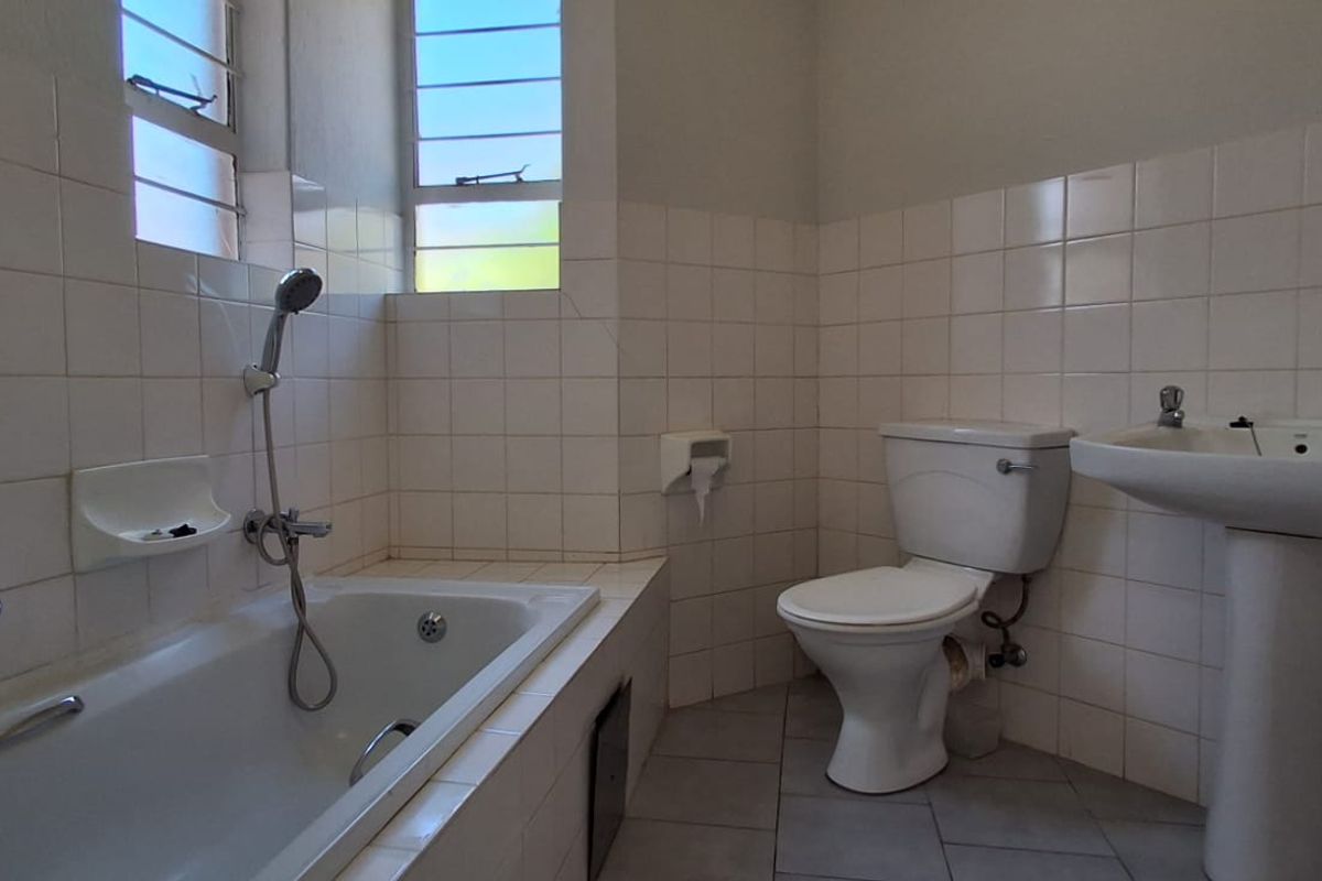 A dated bathroom featuring a built-in bathtub, pedestal basin, and toilet with original wall tiling and louver windows.