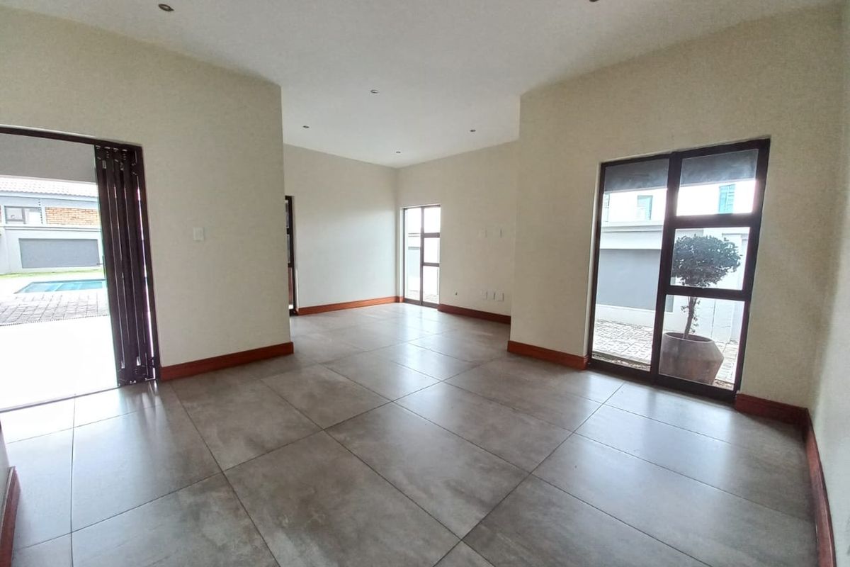 A spacious, empty living area featuring large format floor tiles, recessed lighting, and multiple aluminium-framed glass doors providing access to the exterior.