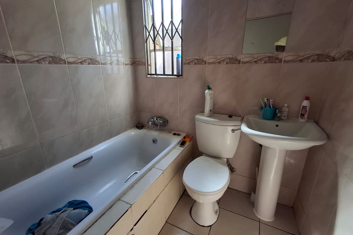 A functional bathroom featuring a bathtub, pedestal basin, and toilet with tiled finishes and security bars on the window.