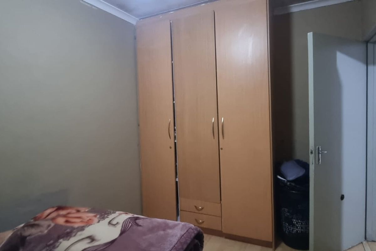 A bedroom featuring a built-in wooden wardrobe and neutral wall finishes, offering a functional space with potential for cosmetic updates.