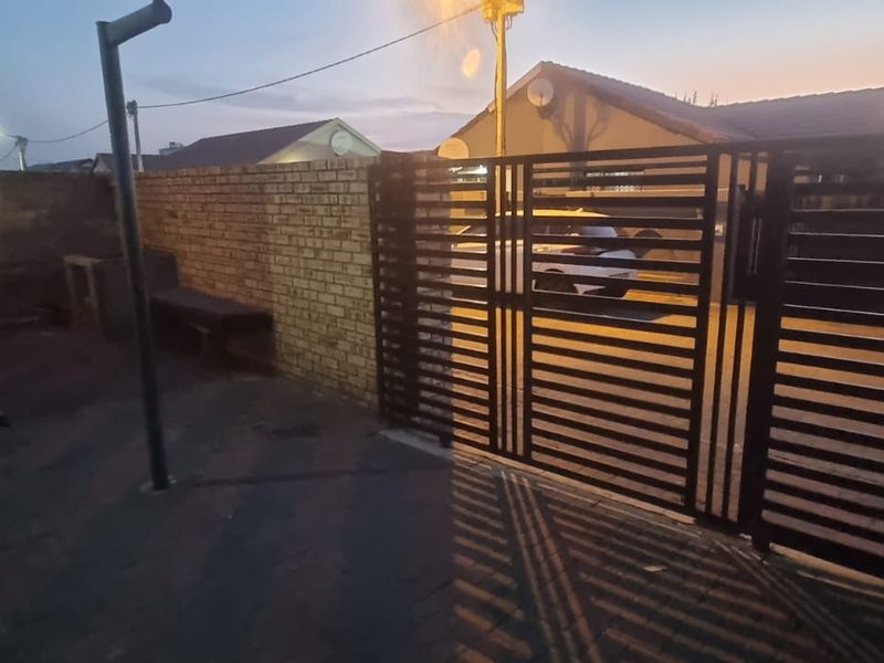 Front exterior view featuring a paved driveway, secure metal gate, and a built-in brick braai area against the boundary wall.
