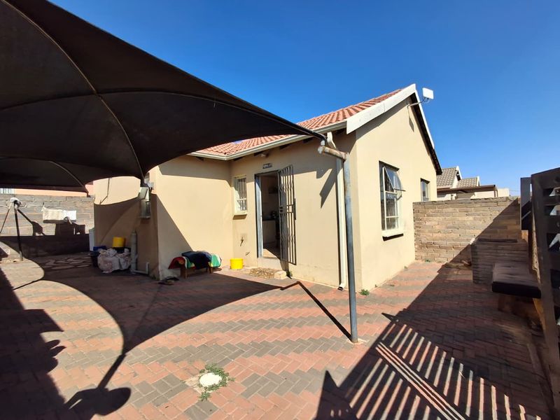 Rear exterior view of the house featuring a paved patio area, shade sail, and brick boundary walling.