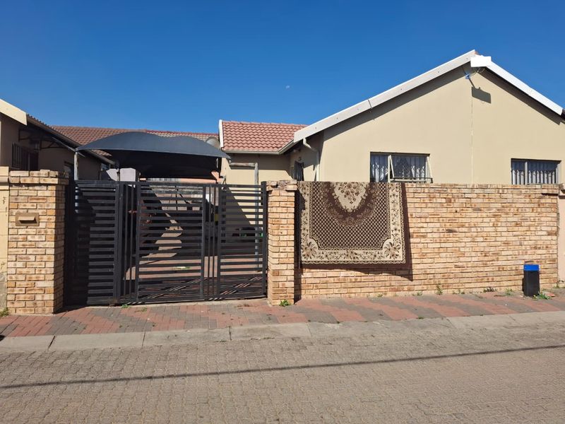 Front exterior view of the property featuring a brick boundary wall, metal driveway gate, and a shade cloth carport.