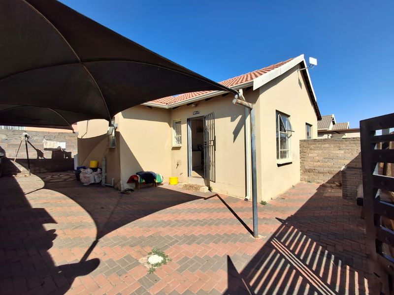 Rear exterior view of the property featuring a paved patio area, shade sail, and secure access point with a brick boundary wall.