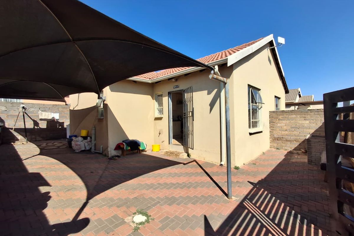 Rear exterior view of the property featuring a paved patio area, shade sail, and secure access point with a brick boundary wall.