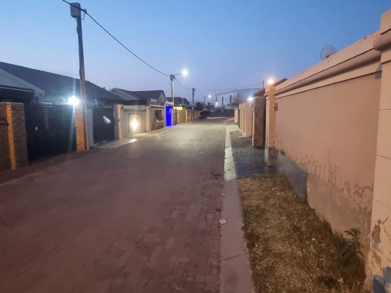 A street-level view of a residential neighborhood at dusk, featuring paved roads and perimeter boundary walls.