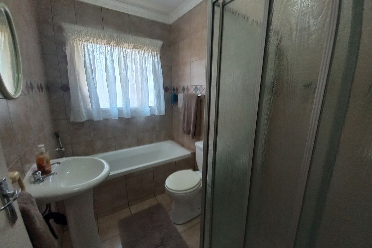A functional bathroom featuring a pedestal basin, built-in bathtub, toilet, and a separate shower enclosure with tiled finishes throughout.