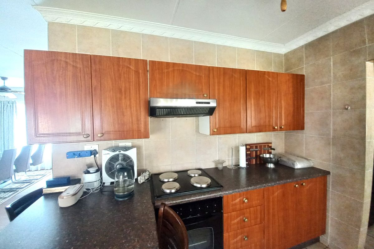 A functional kitchen featuring wood-look cabinetry, dark laminate countertops, a built-in electric oven and hob, and a tiled backsplash.