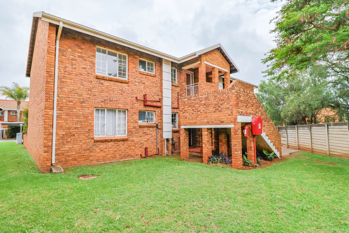 Rear view of a multi-story face brick apartment building featuring an external staircase, balcony, and surrounding communal garden area.