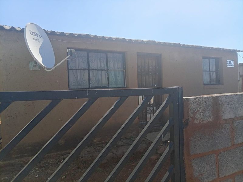 Front exterior view of a single-story house featuring a security gate, security bars on windows, and a satellite dish installation.