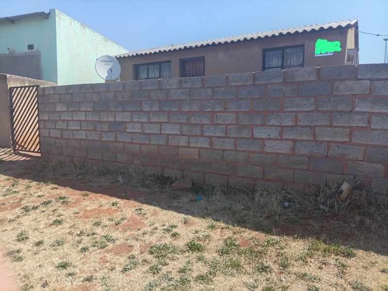 Front view of the property featuring a concrete block boundary wall, metal pedestrian gate, and security bars on the windows.