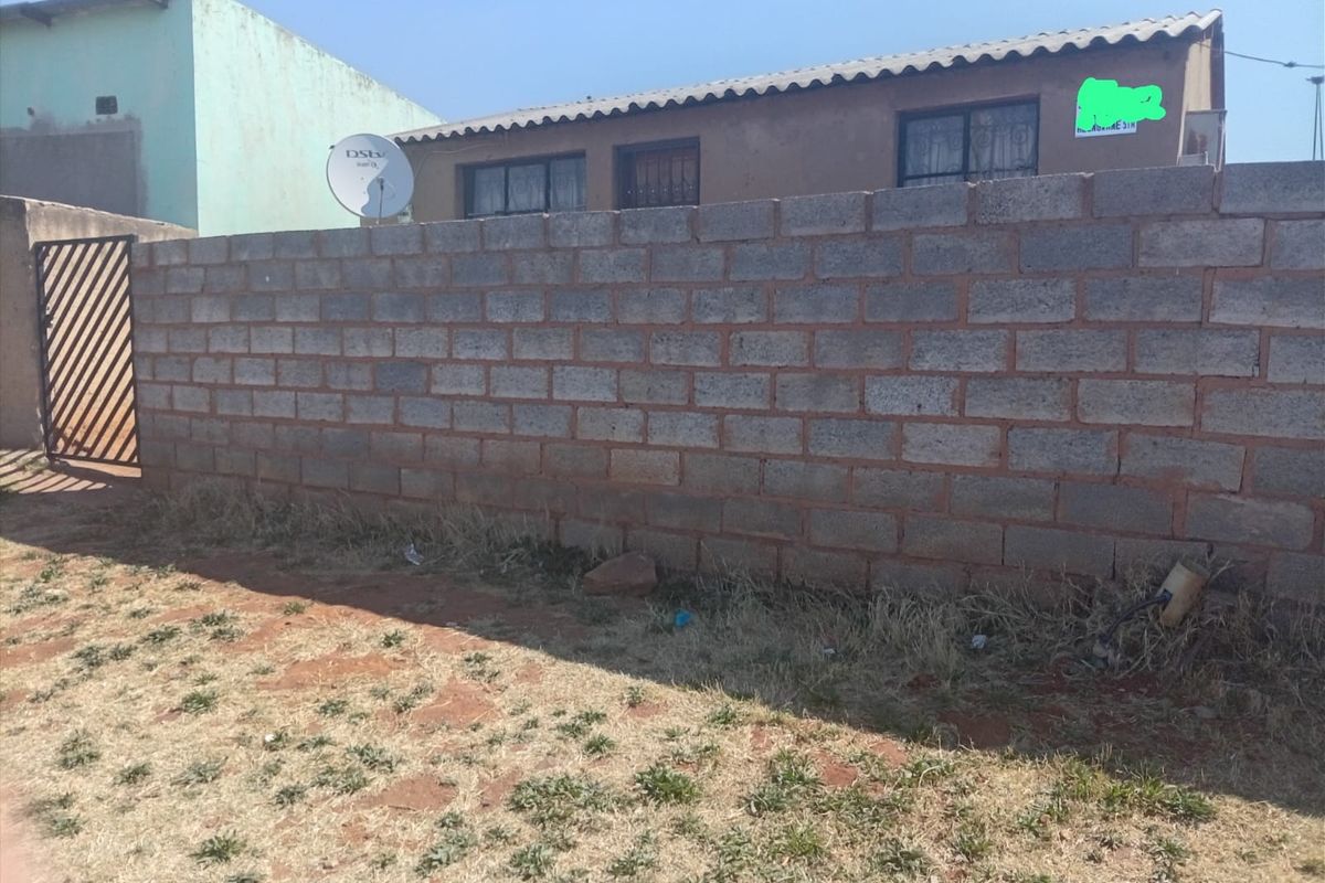 Front view of the property featuring a concrete block boundary wall, metal pedestrian gate, and security bars on the windows.