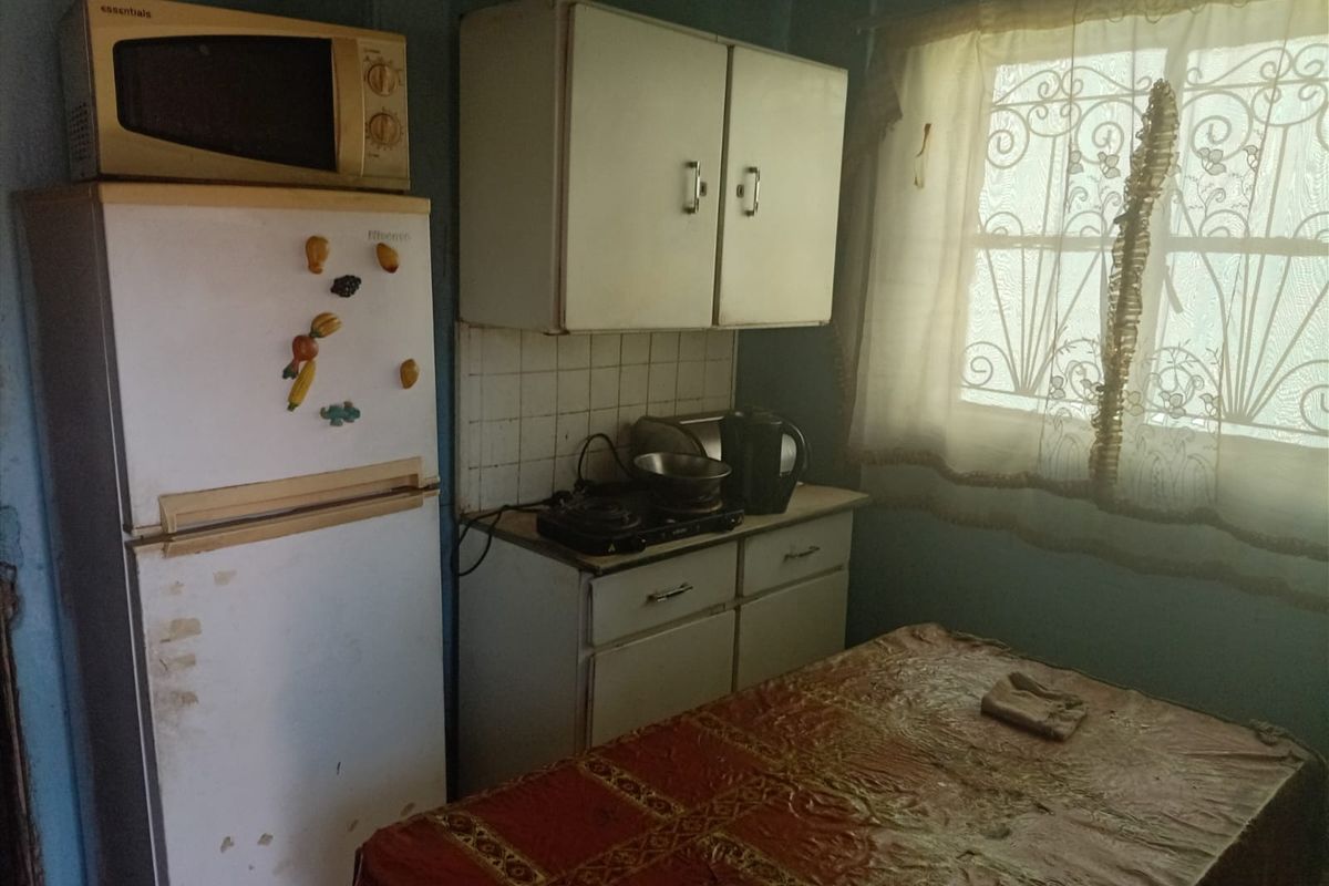 A compact kitchen featuring dated cabinetry, tiled backsplash, and a window with security bars, offering potential for modernization and layout optimization.