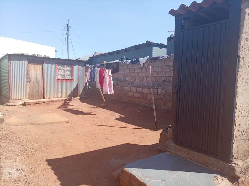 Rear yard area featuring a corrugated metal structure, brick boundary wall, and basic outdoor access steps.