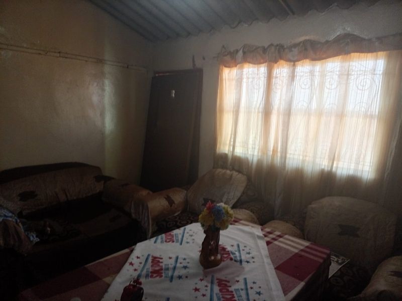 A living room area featuring a window with security bars and an exposed corrugated roof structure, requiring cosmetic updates to improve the interior finish.