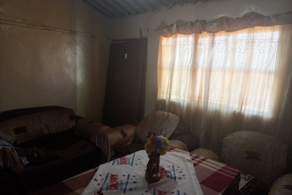 A living room area featuring a window with security bars and an exposed corrugated roof structure, requiring cosmetic updates to improve the interior finish.